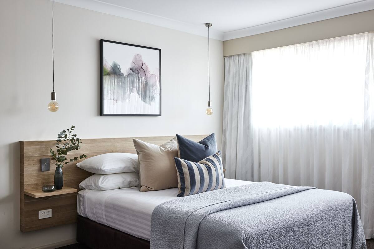 A neatly arranged bedroom with a bed, bedside table, and a framed artwork on the wall.