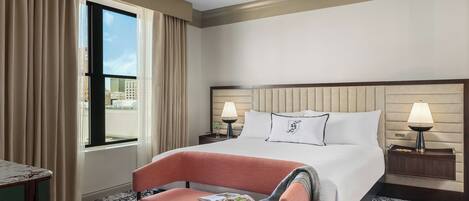 A hotel room with a large bed, two bedside tables, a chair, a window with curtains, and a patterned carpet.