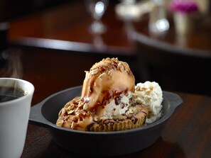 A dessert with ice cream and caramel sauce in a black bowl.