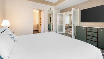 A hotel room with a large bed, a TV, a desk with drawers, a mirror, and a door leading to a bathroom.