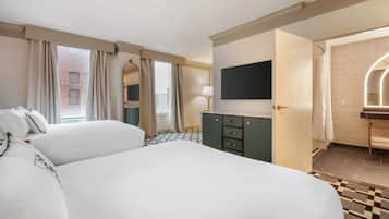 Une chambre d’hôtel avec un grand lit, une commode, un téléviseur fixé au mur et une vue sur la ville par la fenêtre.