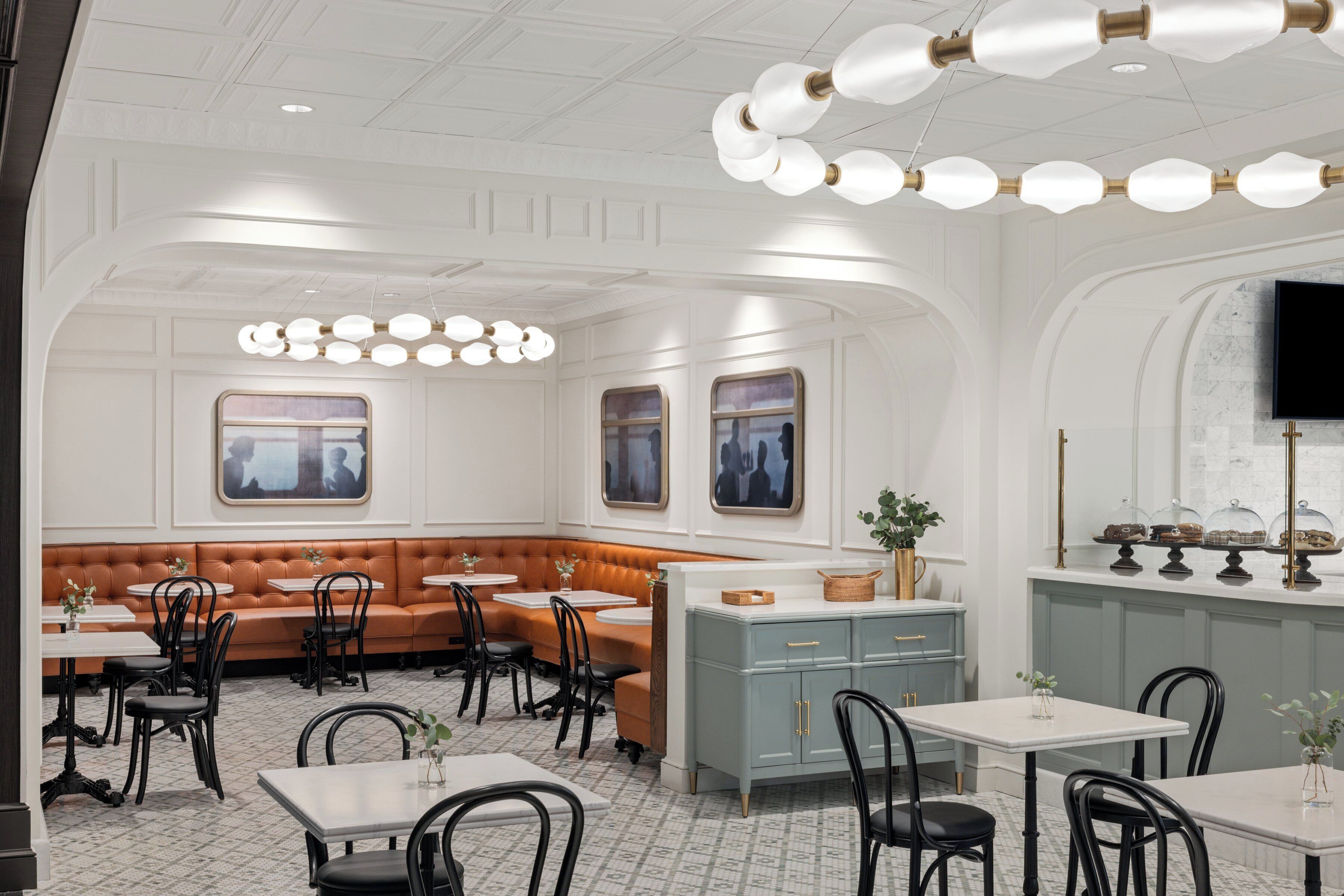 A restaurant with a white interior, featuring a central orange booth, black chairs, and white tables.