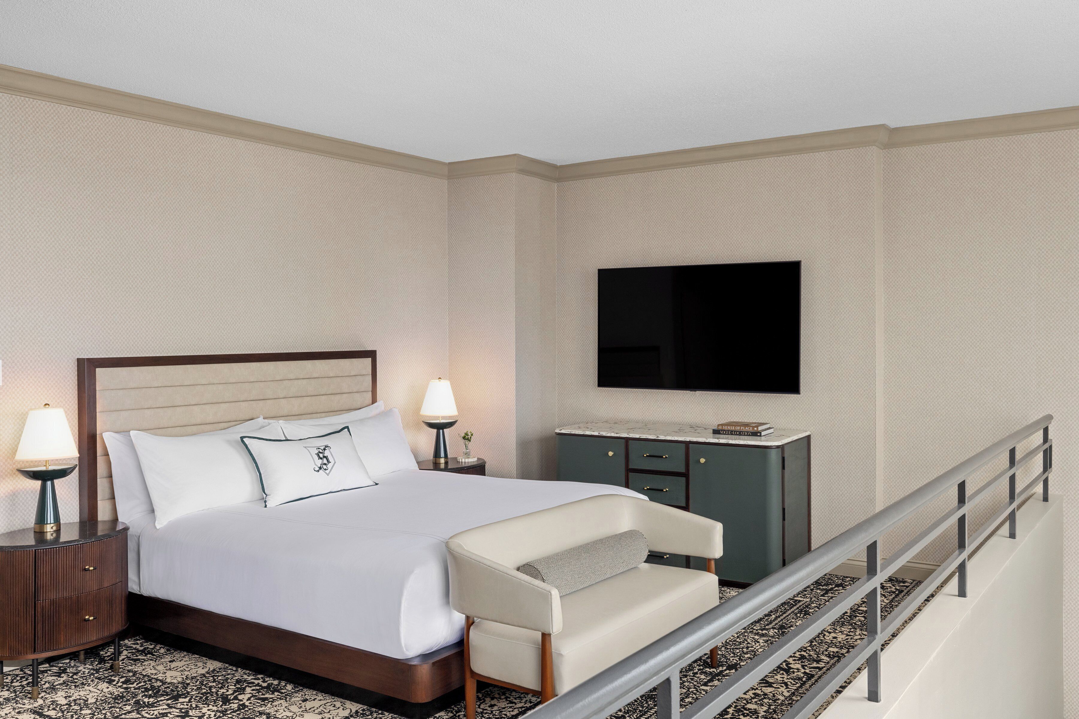 Una habitación de hotel con cama, escritorio, silla, televisor y barandilla.