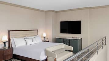 Quarto de hotel com cama, escrivaninha, cadeira, televisão e corrimão.