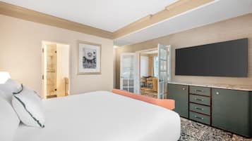 A hotel room with a large bed, a flat-screen TV mounted on the wall, a wooden cabinet with drawers, and a door leading to a bathroom.