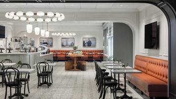 Un restaurant moderne doté d’un espace de restauration central, de murs blancs et d’un mélange de tables et de banquettes.
