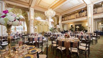 A grand ballroom with ornate chandeliers, tiered seating, and floral centerpieces.