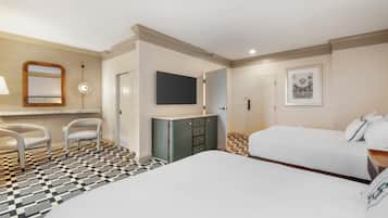 A hotel room with a checkered floor, a bed, a desk with a chair, a wardrobe, a mirror, and a flat-screen TV.