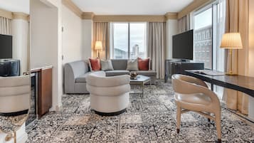 A hotel room with a sofa, armchair, desk, and TV.
