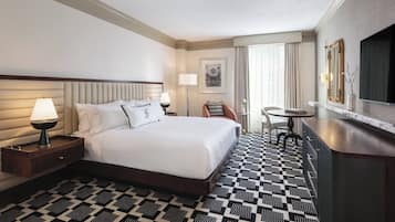 Habitación de hotel con una cama grande, mesitas de noche con lámparas, un escritorio, una silla y un televisor.