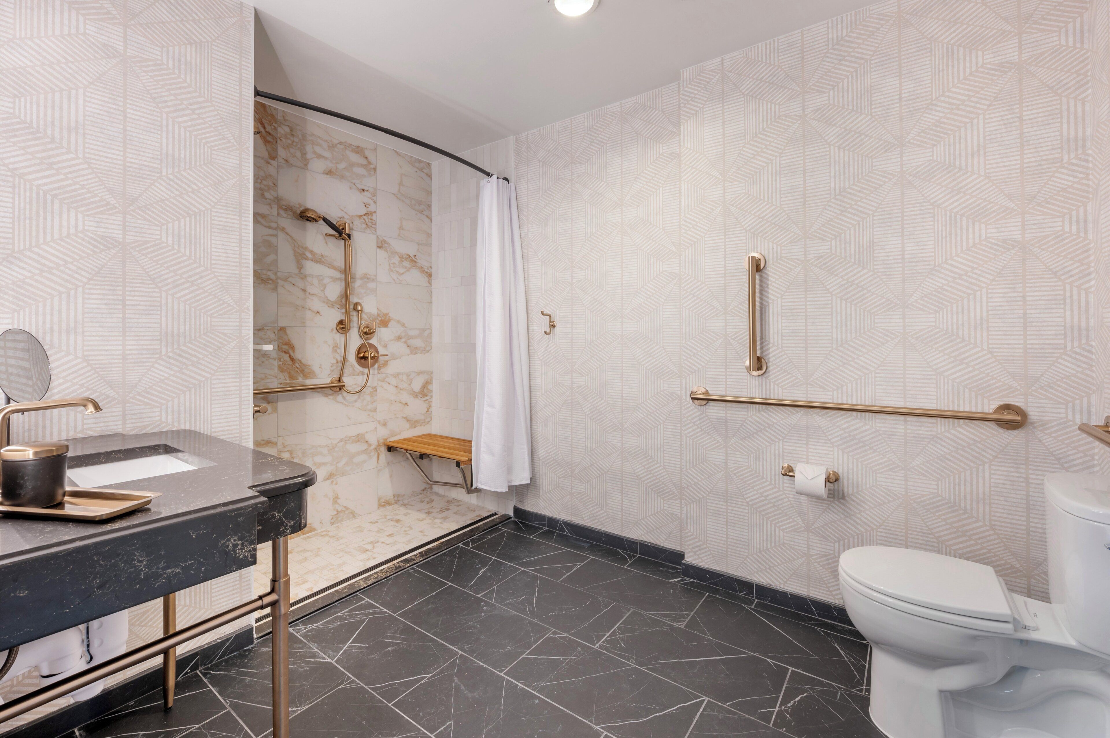 A modern bathroom with a black marble sink, gold fixtures, a white toilet, and a shower with a marble wall.