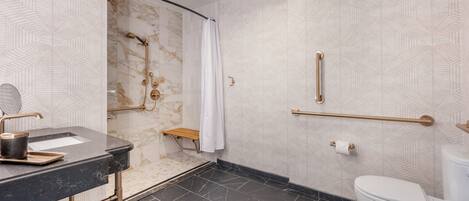 A modern bathroom with a black marble sink, gold fixtures, a white toilet, and a shower with a marble wall.