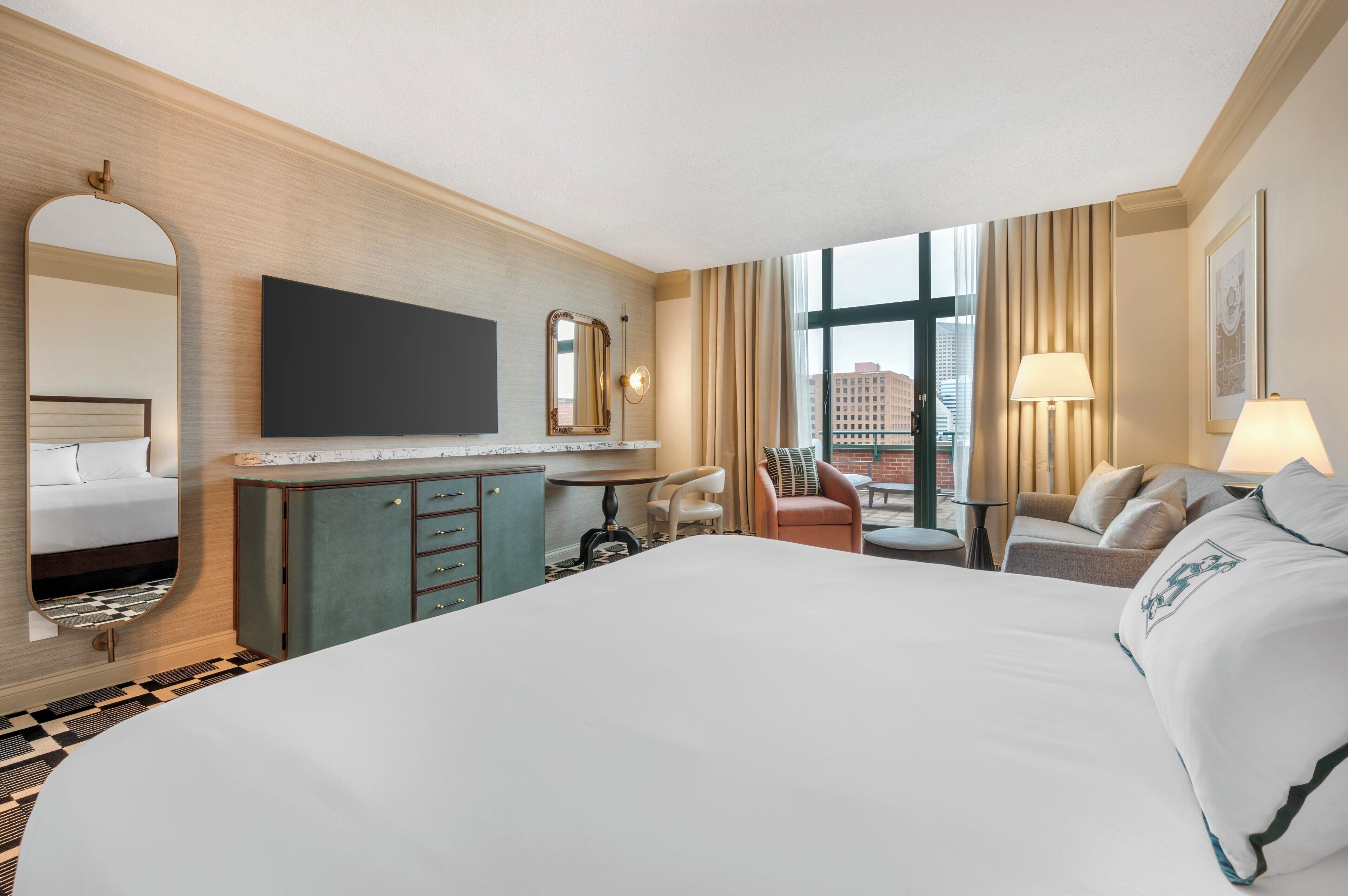 A hotel room with a large bed, a desk with a chair, a television, a mirror, and a window with curtains.
