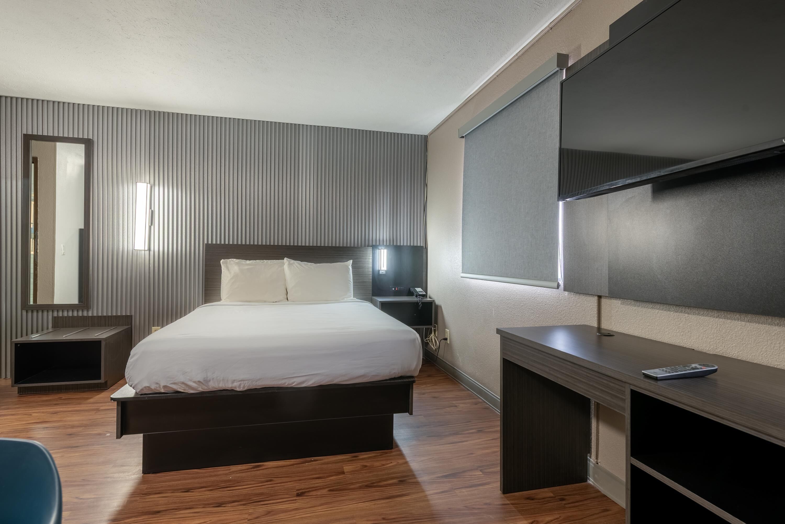 A modern hotel room with a large bed, a desk, a TV, and a mirror.
