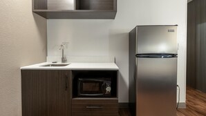 Una cocina compacta con microondas integrado, un refrigerador de acero inoxidable y un mueble de madera con un cajón.