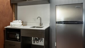 Una cocina compacta con microondas integrado, un lavamanos y un refrigerador de acero inoxidable.