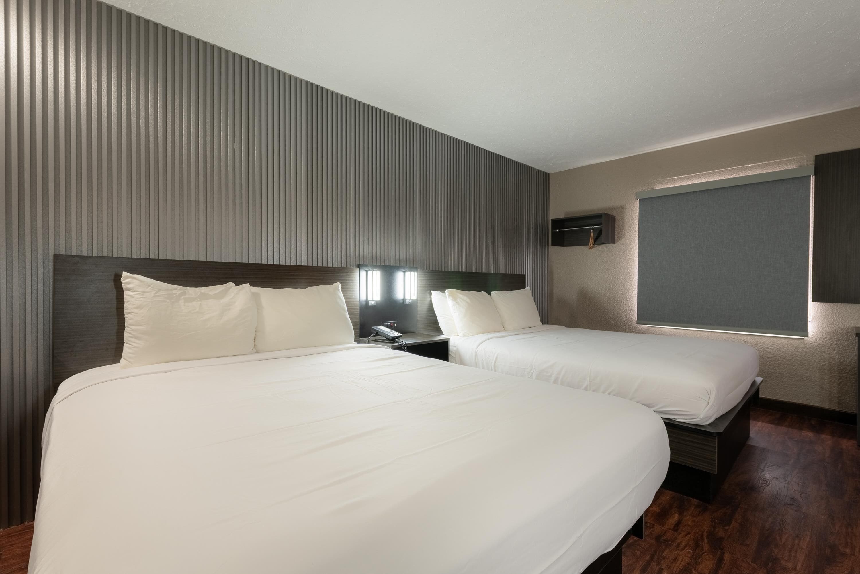 A hotel room with two beds, a wooden floor, a sloped ceiling, and a wall-mounted TV.