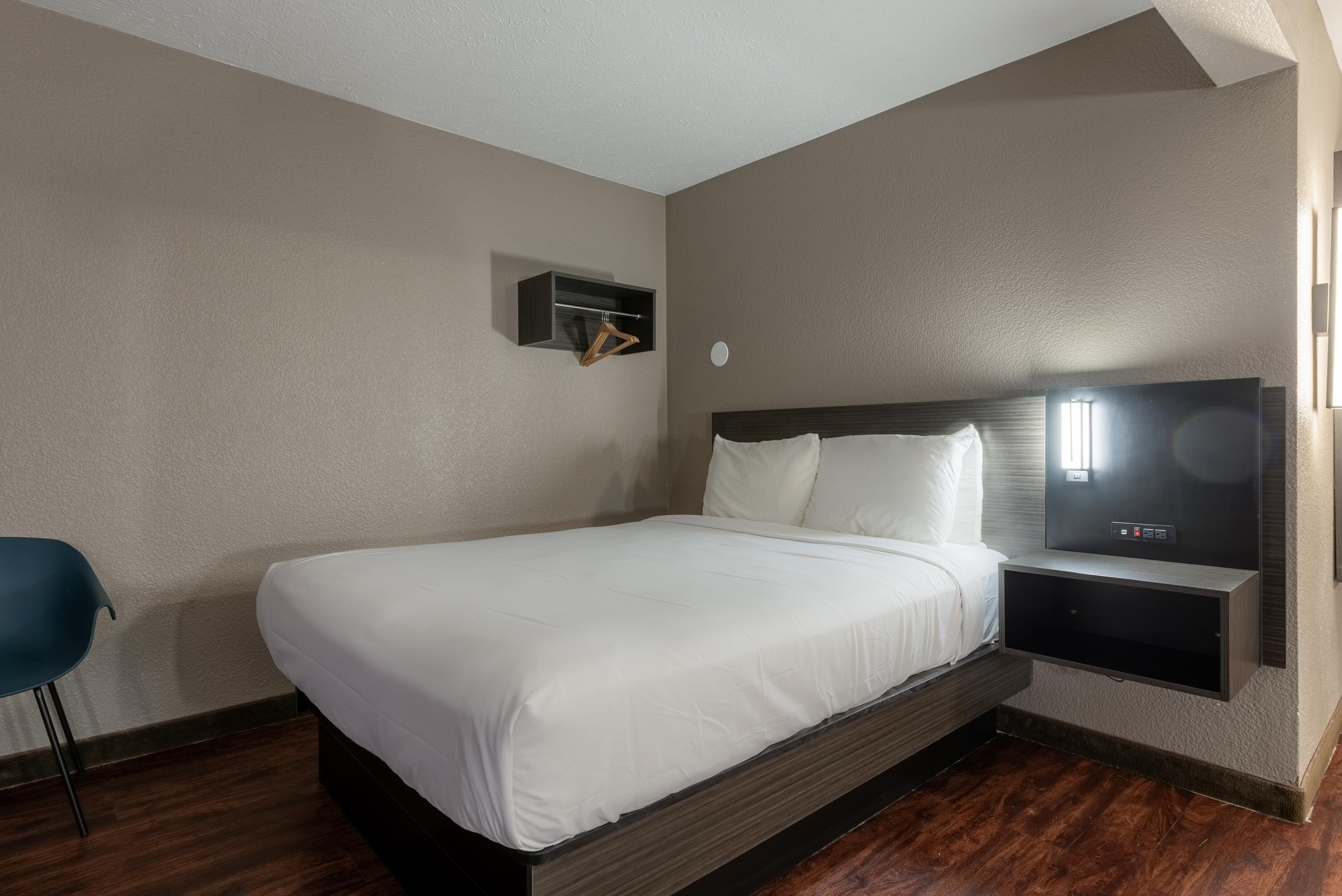 A hotel room with a bed, a TV, a small shelf, and a chair.