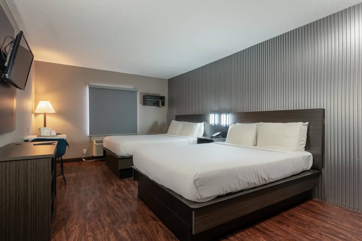 Een hotelkamer met twee bedden, een bureau, een stoel, een televisie en een raam.