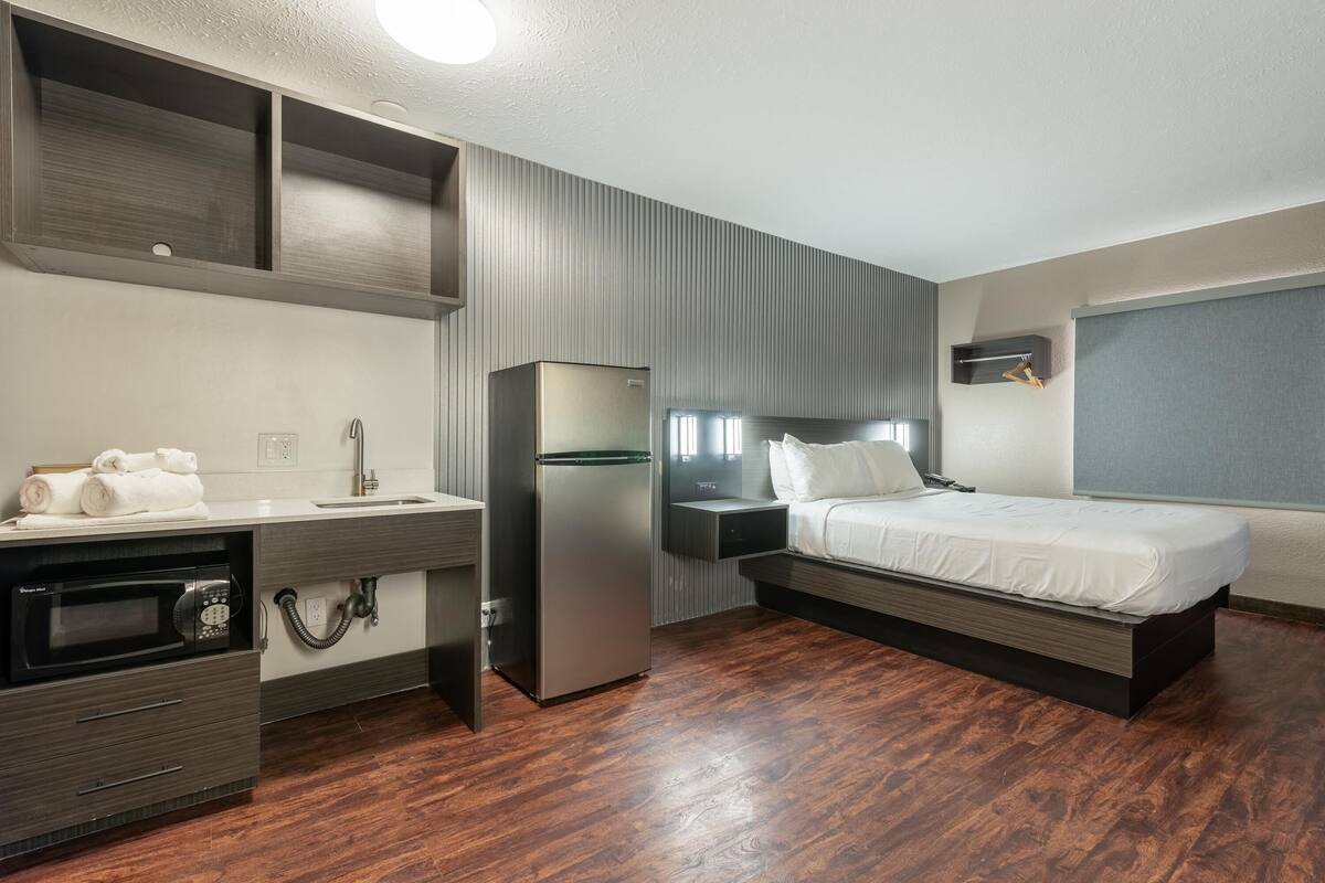 Een moderne hotelkamer met een kitchenette, een bed en een groot raam.