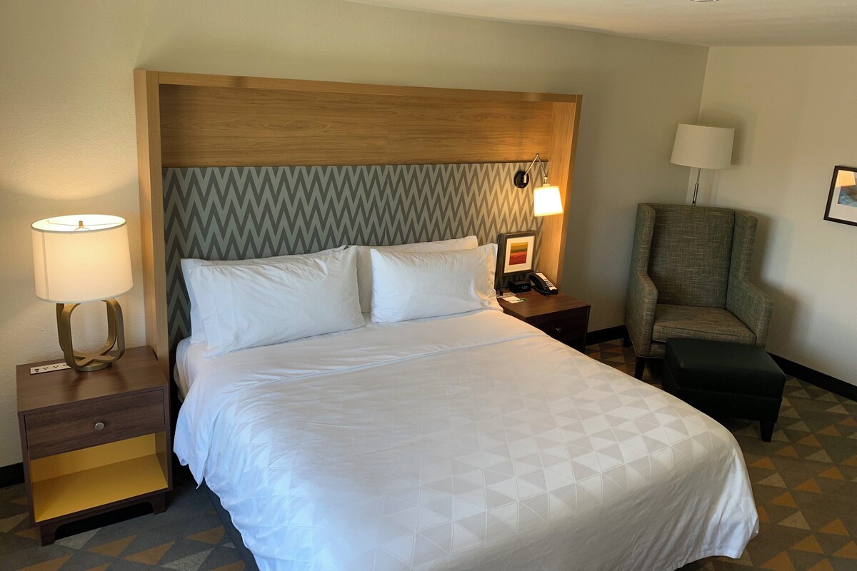 Une chambre d’hôtel avec un grand lit, une table de chevet avec une lampe, une chaise et un bureau avec un téléphone.