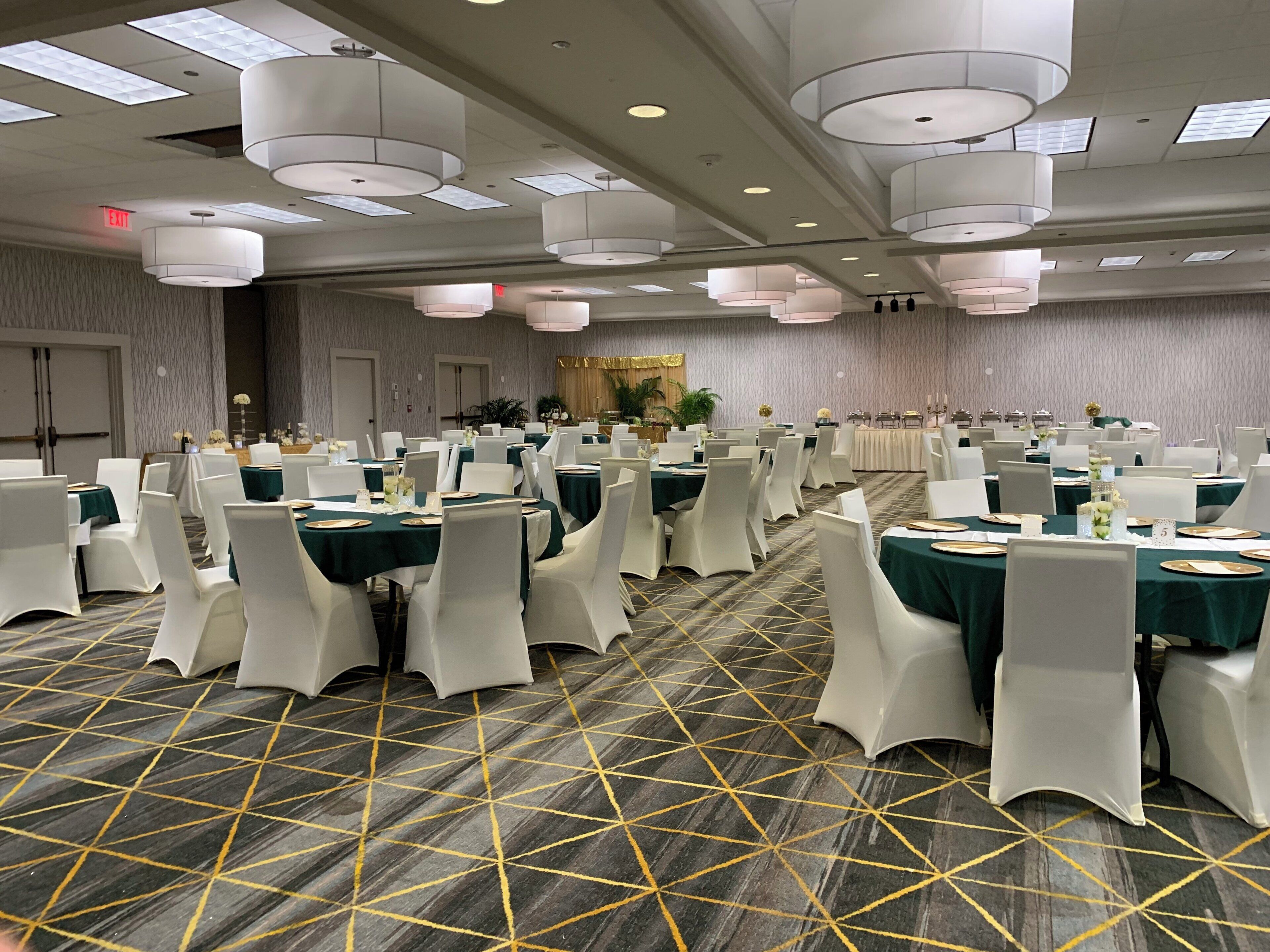A banquet hall with round tables, white chairs, and green tablecloths.
