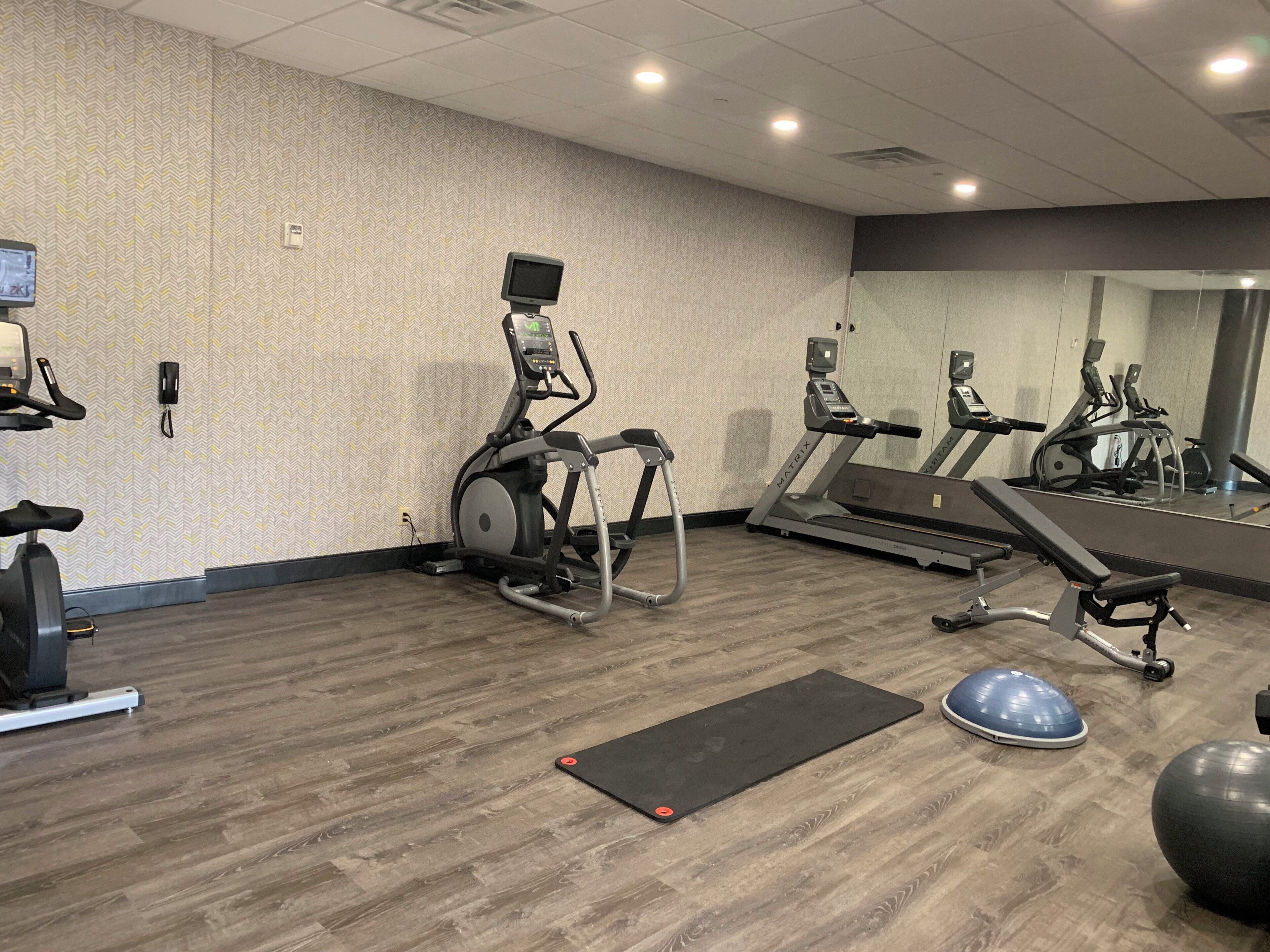 Ein Fitnessraum mit verschiedenen Trainingsgeräten, darunter Laufbänder, ein Crosstrainer und ein stationäres Fahrrad.