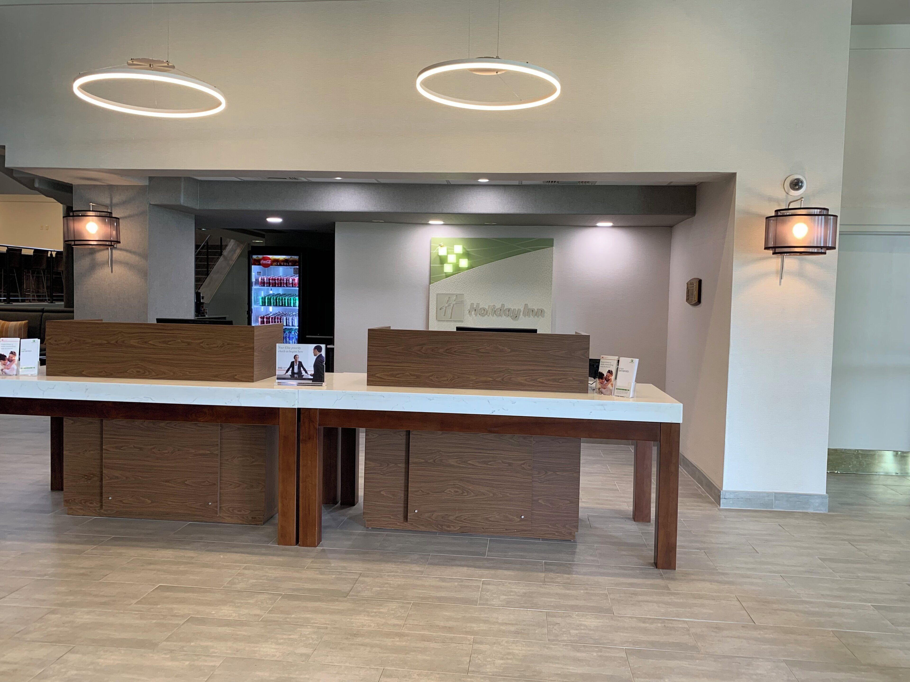 A reception desk with a modern design, two overhead circular light fixtures, and a wall-mounted security camera.