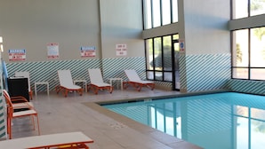 Une piscine intérieure dotée de chaises longues et d’un sol carrelé.