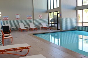 An indoor swimming pool with lounge chairs and a tiled floor.