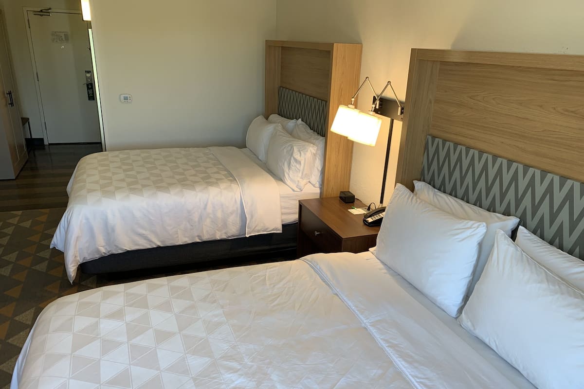 Habitación de hotel con dos camas, una mesita de noche, una lámpara y una puerta.