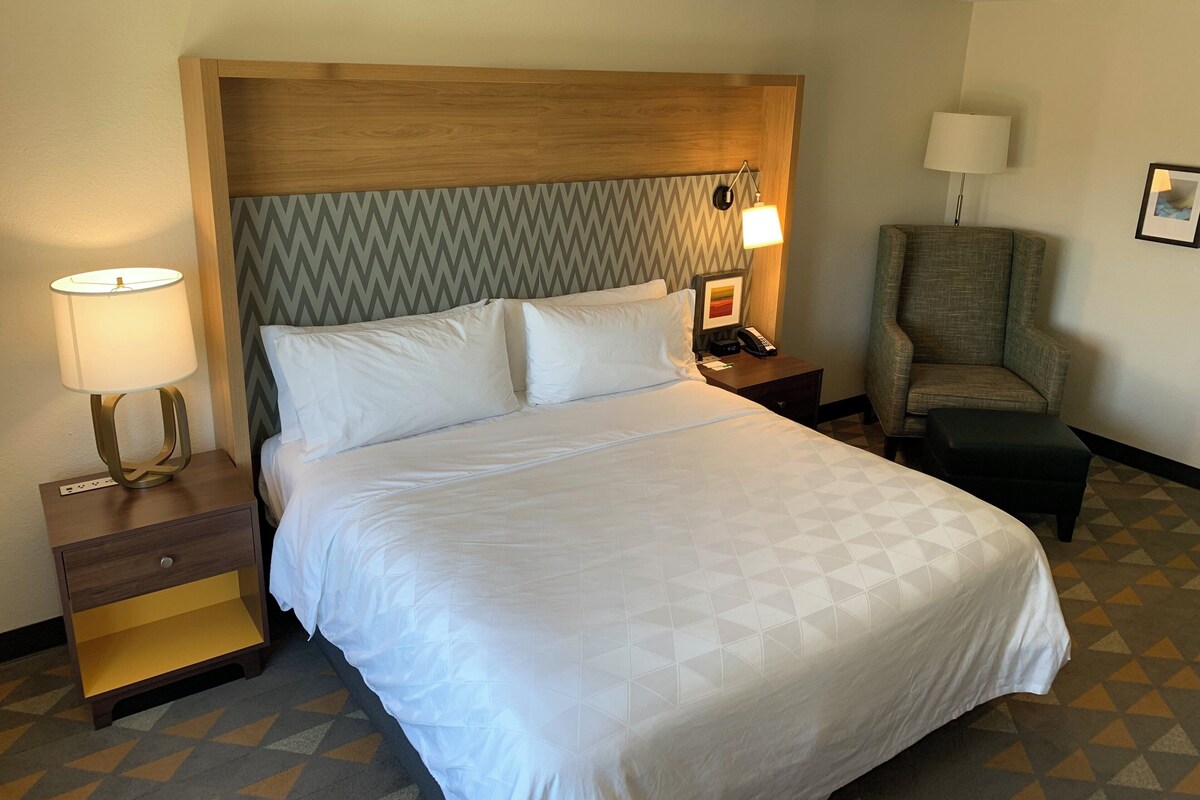 Une chambre d’hôtel avec un grand lit, une table de chevet avec une lampe, une chaise et un téléphone fixé au mur.