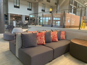 A modern interior with a sectional sofa, a round wooden table, and a glass railing overlooking a dining area.