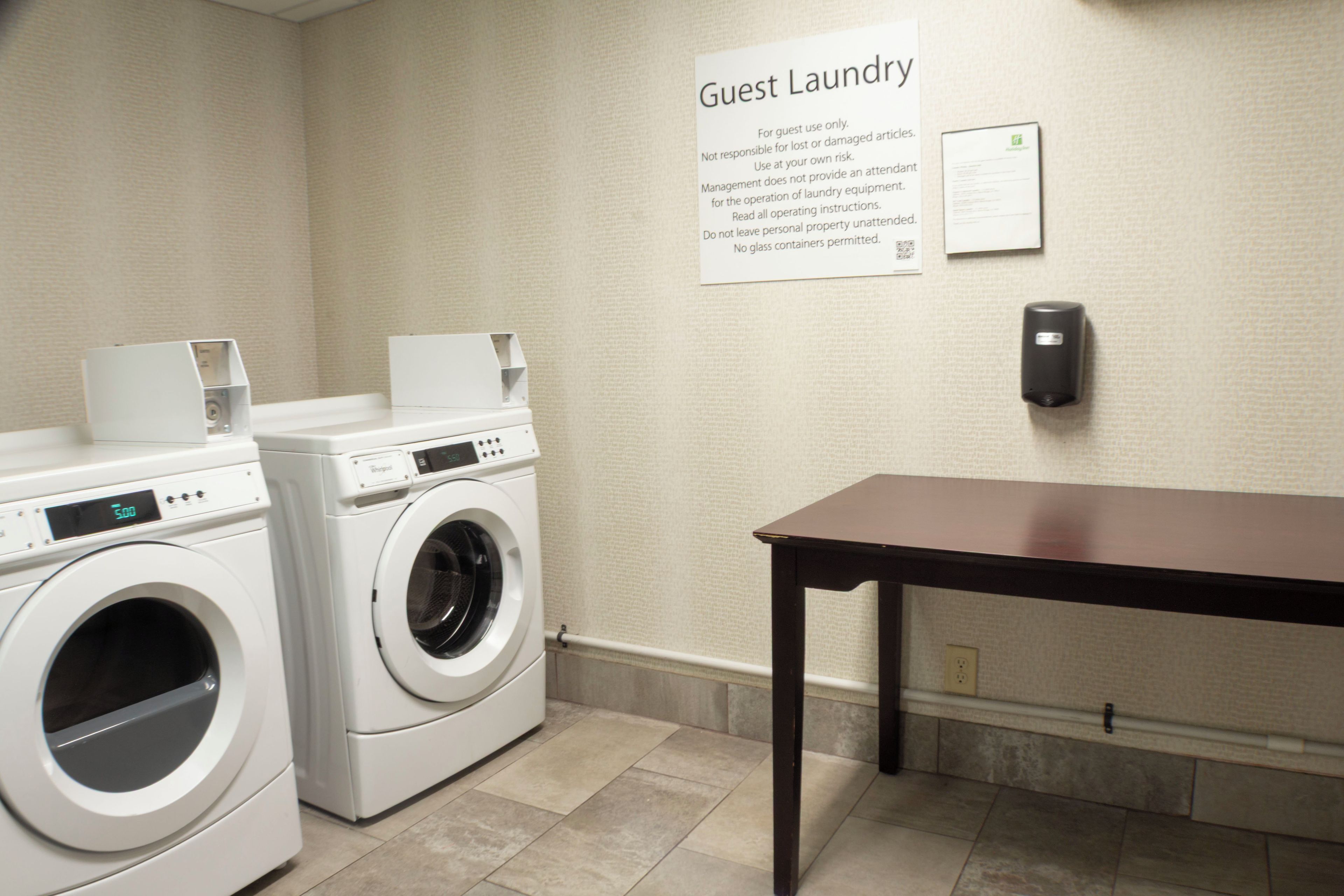 A guest laundry area with two washing machines, a table, and a sign detailing usage instructions.
