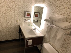 Une salle de bain avec un lavabo blanc, un miroir, des toilettes et un porte-serviettes avec des serviettes pliées.