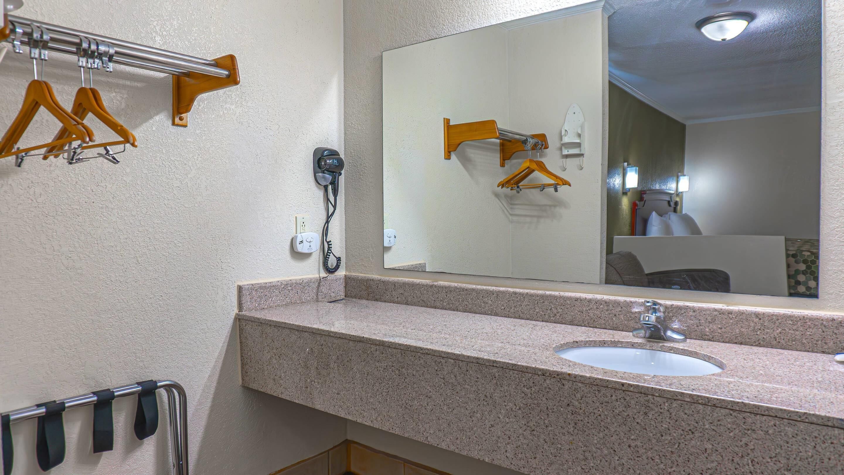 Une salle de bain avec un comptoir en granit, un lavabo, un miroir et des cintres en bois sur un porte-cintres.