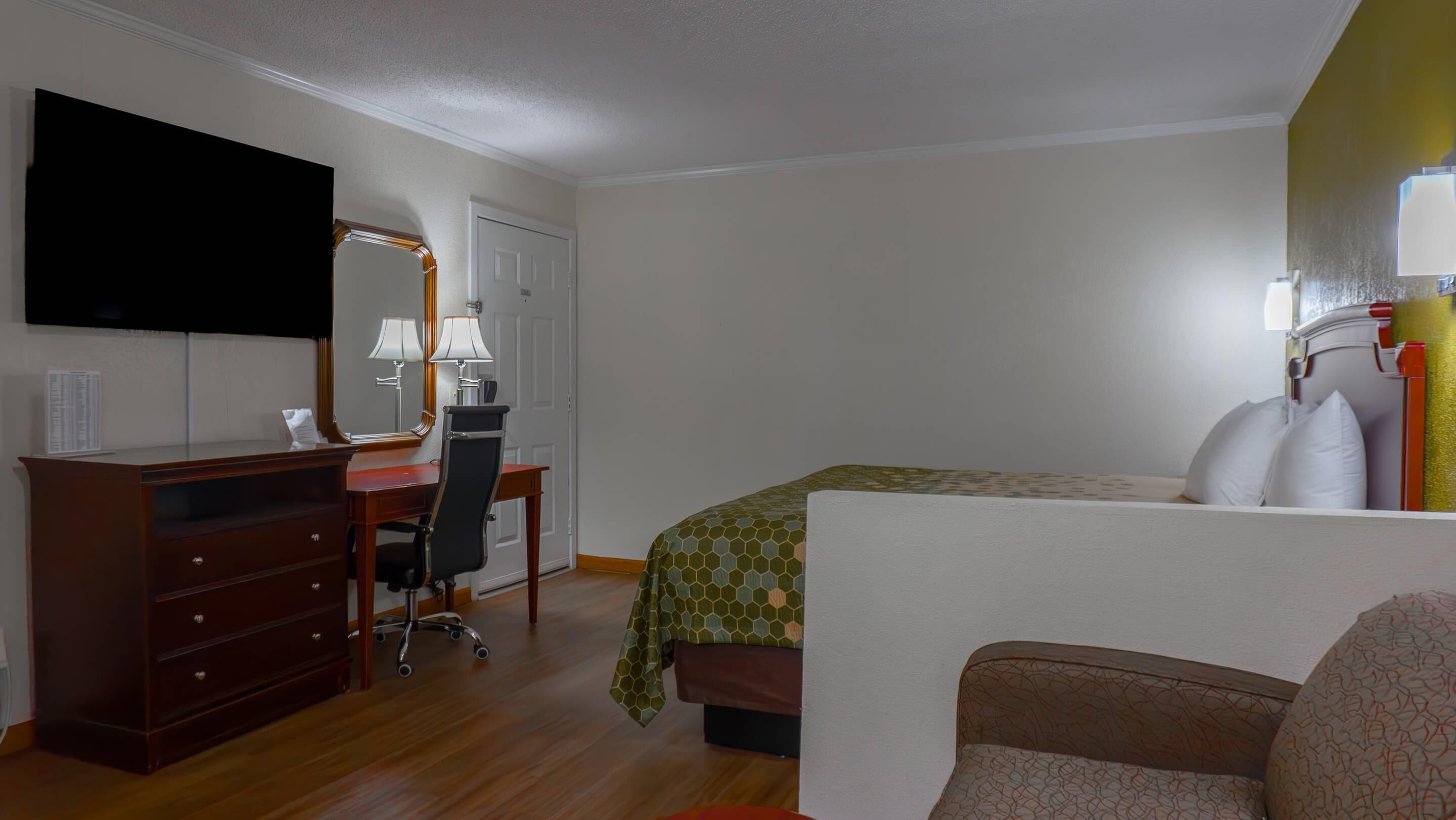 Habitación de hotel con cama, escritorio, silla, televisor y espejo.