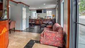 A hotel lobby with a reception desk, a sofa, a coffee station, and a dining area with chairs and tables. - Rodeway Inn & Suites Fort Jackson (Columbia)