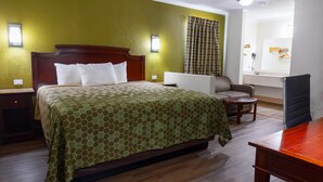 A hotel room with a large bed, a chair, a small table, and a mirror. - Rodeway Inn & Suites Fort Jackson (Columbia)