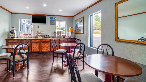 A hotel room with a wooden dining area, a kitchen counter, and a large window providing a view of the outdoors. - Rodeway Inn & Suites Fort Jackson (Columbia)