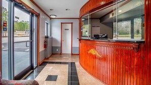 A reception area with a wooden reception desk, a glass door entrance, and a tiled floor. - Rodeway Inn & Suites Fort Jackson (Columbia)