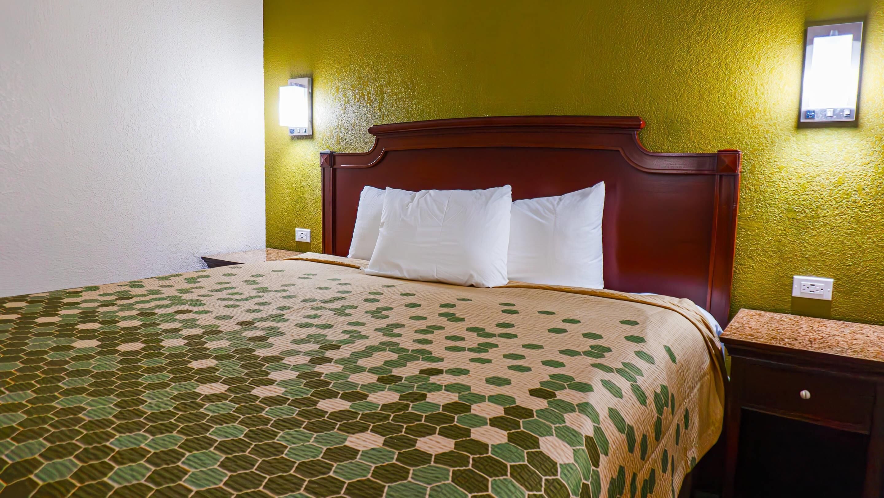 A hotel room with a bed, green walls, and a wooden headboard.