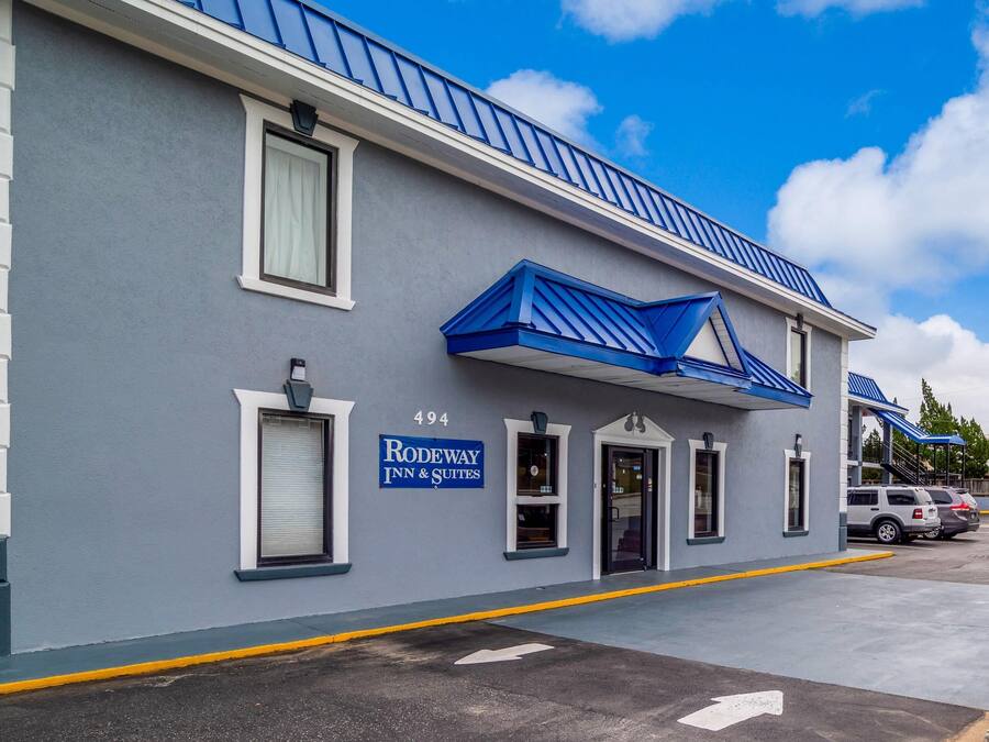 A hotel named "Rodeway Inn & Suites" with a blue and white exterior, numbered 494, and a parking area with cars.
