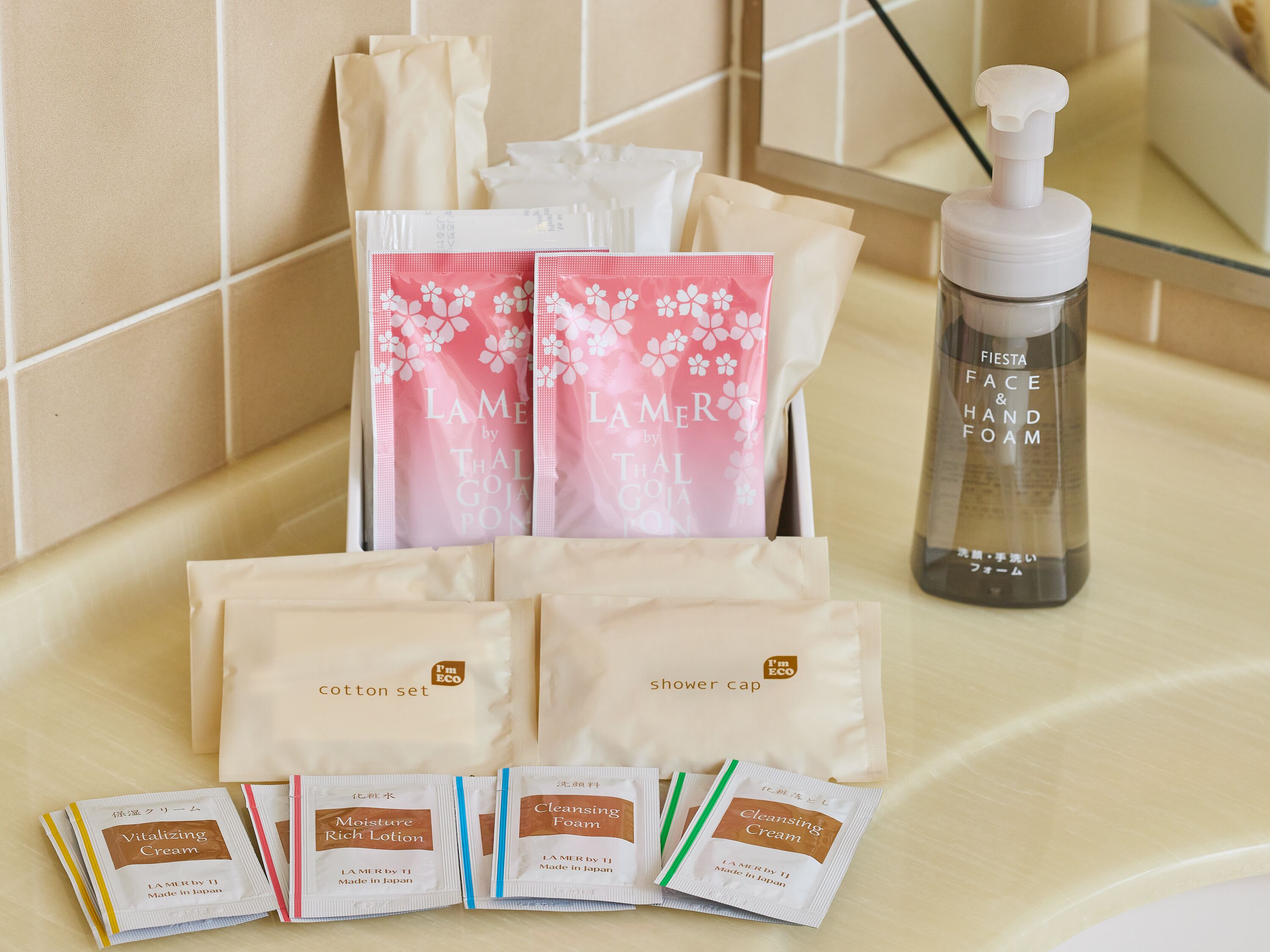 Una encimera de baño con diversos artículos de aseo, incluyendo una botella de espuma para manos y rostro, varias cofias para ducha y múltiples sobres de espuma limpiadora y loción hidratante.
