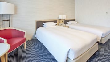 Une chambre d’hôtel avec deux lits, une chaise rouge, un bureau et une lampe.
