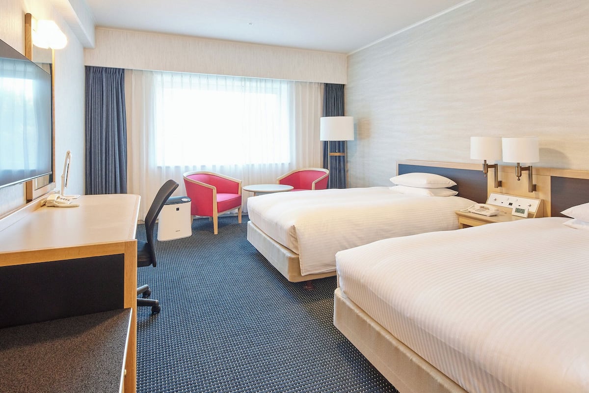 Ein Hotelzimmer mit zwei Betten, einem Schreibtisch, einem Stuhl, einem Fernseher und einem Nachttisch mit Lampe.