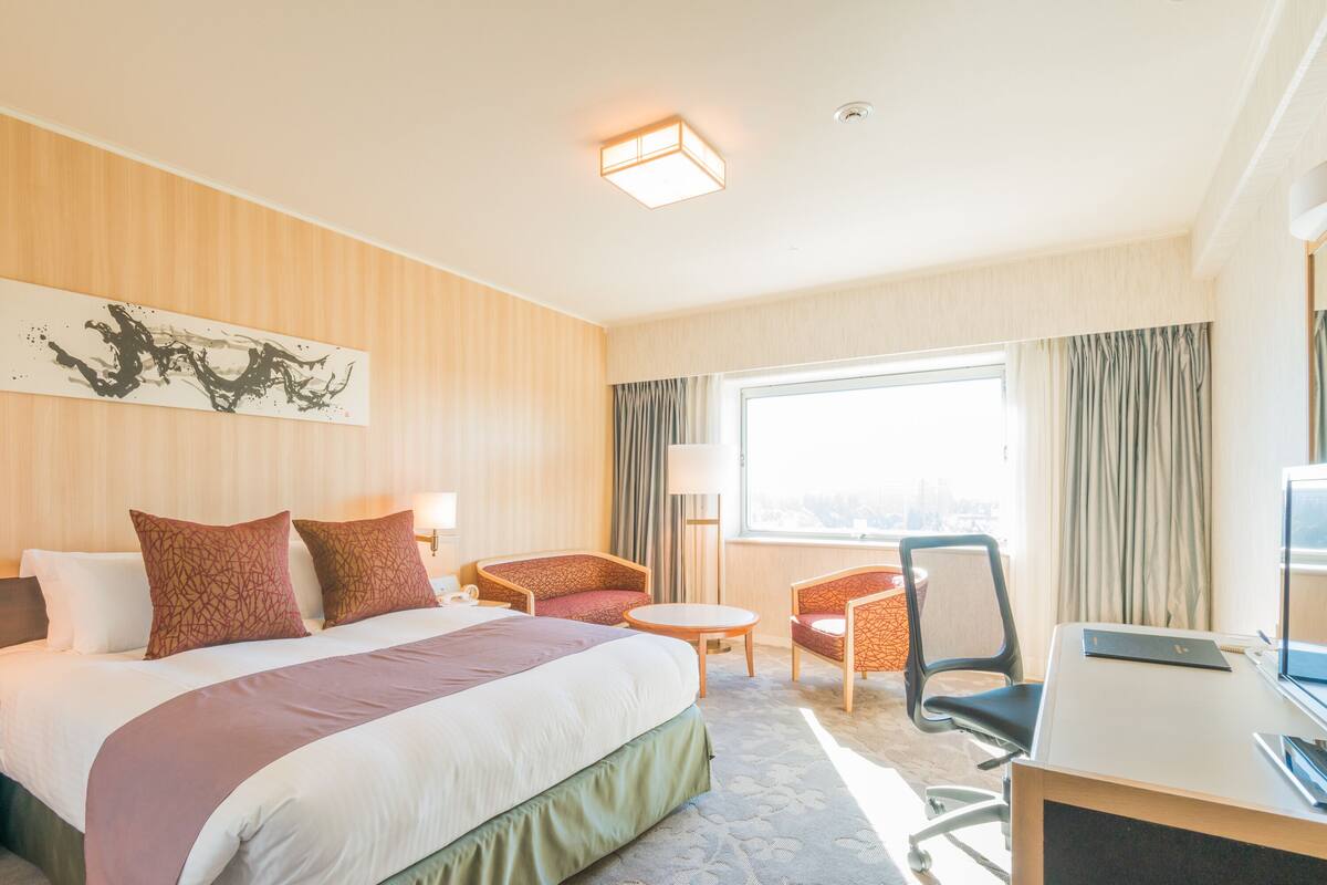 Ein Hotelzimmer mit einem großen Bett, zwei Sesseln, einem Schreibtisch und einem großen Fenster.