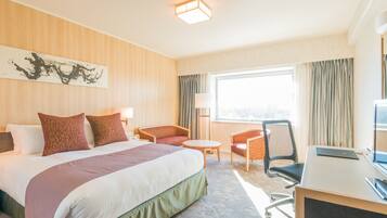 A hotel room with a large bed, two armchairs, a desk, and a large window.