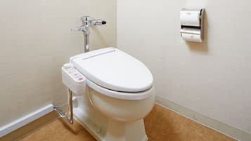 A modern toilet with a control panel, a wall-mounted toilet paper dispenser, and a visible pipe.