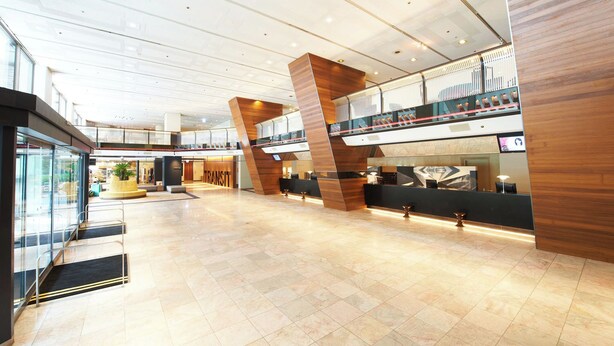 Un hall d’entrée spacieux au design moderne, doté d’un atrium central, d’un comptoir d’accueil et d’un escalier apparent menant à un niveau supérieur.
